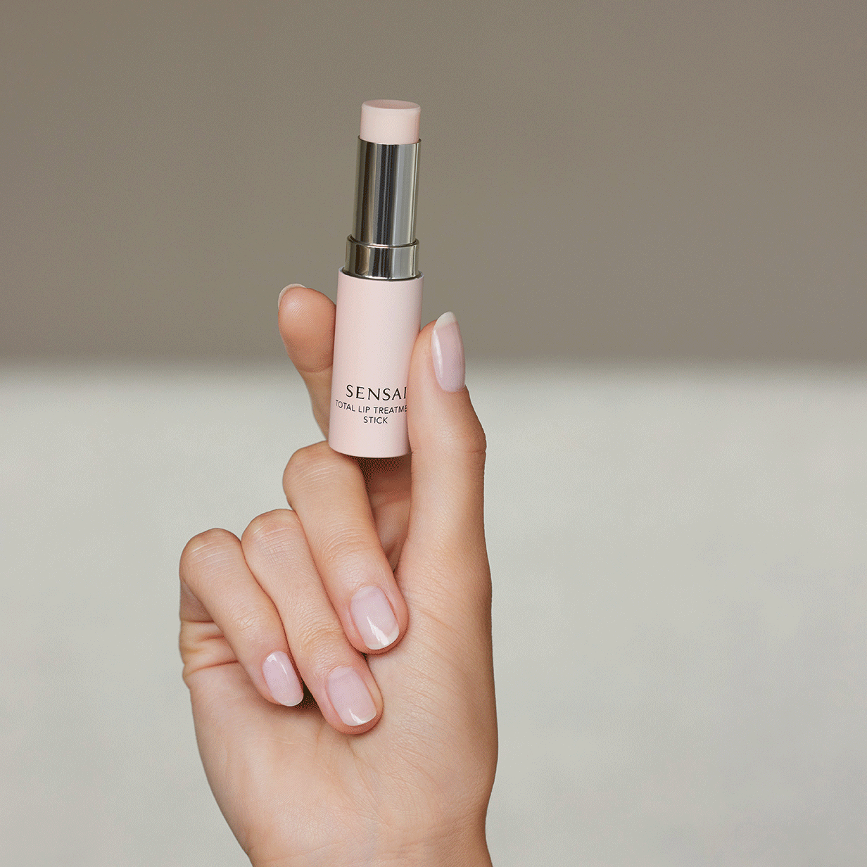 Total Lip Treatment Stick di SENSAI in mano seguito da Total Lip Treatment su dei libri impilati sopra un tavolo 